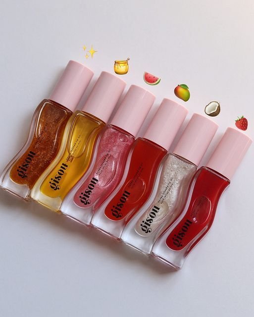 Huile pour les lèvres Gisou Honey Gold posée sur une surface dorée, mise en valeur par une lumière douce